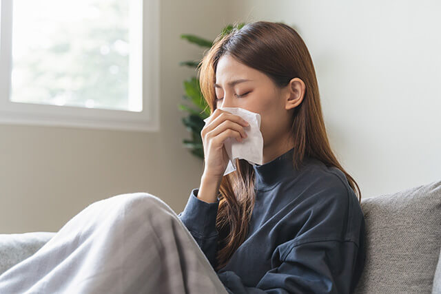 鼻をティッシュペーパーでおさえる女性